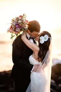 Sun shining through bride's bouquet while bride and groom kiss on lava